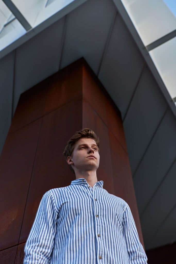 man in blue and white striped dress shirt standing near brown wall