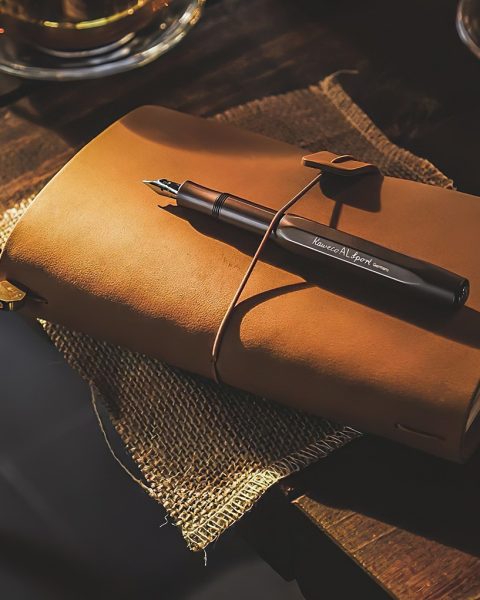 Een elegante vulpen liggend naast een hardcover notitieboek op een verzorgd houten bureau