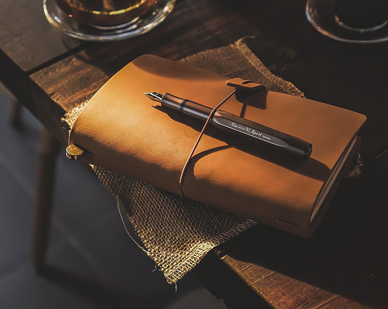 Een elegante vulpen liggend naast een hardcover notitieboek op een verzorgd houten bureau
